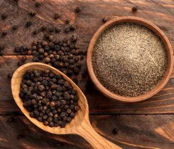 Black peppercorns in a spoon and black ground pepper in a plate close-up on a wooden background. Top view