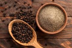 Black peppercorns in a spoon and black ground pepper in a plate close-up on a wooden background. Top view