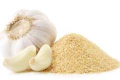 A pile of ground garlic and a head of garlic with cloves close-up on a white background. Isolated