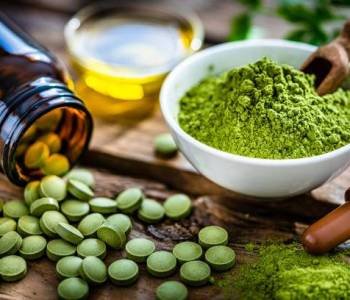 Nutritional supplement: Moringa powder in a white bowl and Moringa capsules spilling out a bottle shot on rustic wooden table. High resolution 42Mp studio digital capture taken with Sony A7rII and Sony FE 90mm f2.8 macro G OSS lens