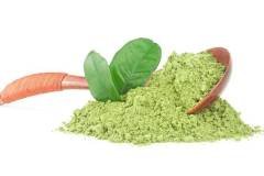 Wooden spoon with powdered matcha green tea and fresh tea leaves, white background.