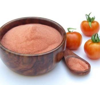 Tomato powder in a wooden bowl with fresh tomatoes isolated on white background